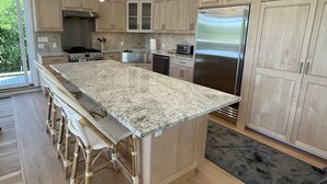 Una cocina amplia con una isla grande, armarios de madera, electrodomésticos de acero inoxidable y una lámpara colgante de diseño moderno.