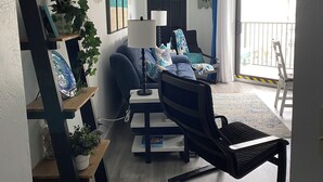 Una sala de estar con un sofá, una silla, una mesa de centro, una lámpara y estanterías con plantas.