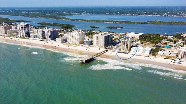 Vista aérea de una zona costera con edificios altos, un muelle que se adentra en el agua y una playa y océano despejados.