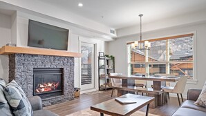 Ein modernes Wohnzimmer mit Kamin aus Stein, einem flachbildfernseher darüber und einem Essbereich mit Holztisch und Stühlen.