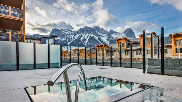 Ein Pool auf dem Dach mit Glasgeländer, moderne Gebäude und schneebedeckte Berge im Hintergrund.