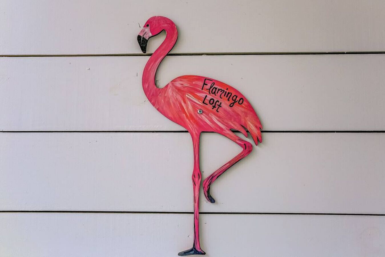 Vaaleanpunainen flamingo-koriste, jossa on teksti ”Flamingo Loft”, valkoisella puuseinällä.
