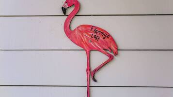 Vaaleanpunainen flamingo-koriste, jossa on teksti ”Flamingo Loft”, valkoisella puuseinällä.