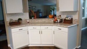 Uma cozinha de canto com armários brancos, bancada de granito e uma pia pequena.