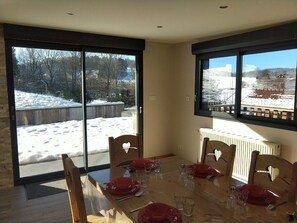 A dining room with a table set for four, large windows, and a view of a snowy landscape. - Mountain cabin for 12 people near Gérardmer (Gerbépal)