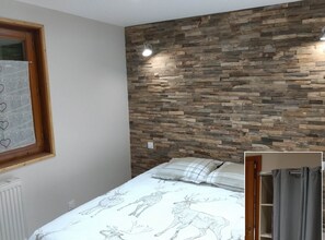A bedroom with a bed, a window with a curtain, a wall with a wooden plank design, and a light fixture. - Mountain cabin for 12 people near Gérardmer (Gerbépal)