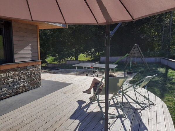 Een houten terras met een tafel, stoelen, een schommel en een stenen muur.
