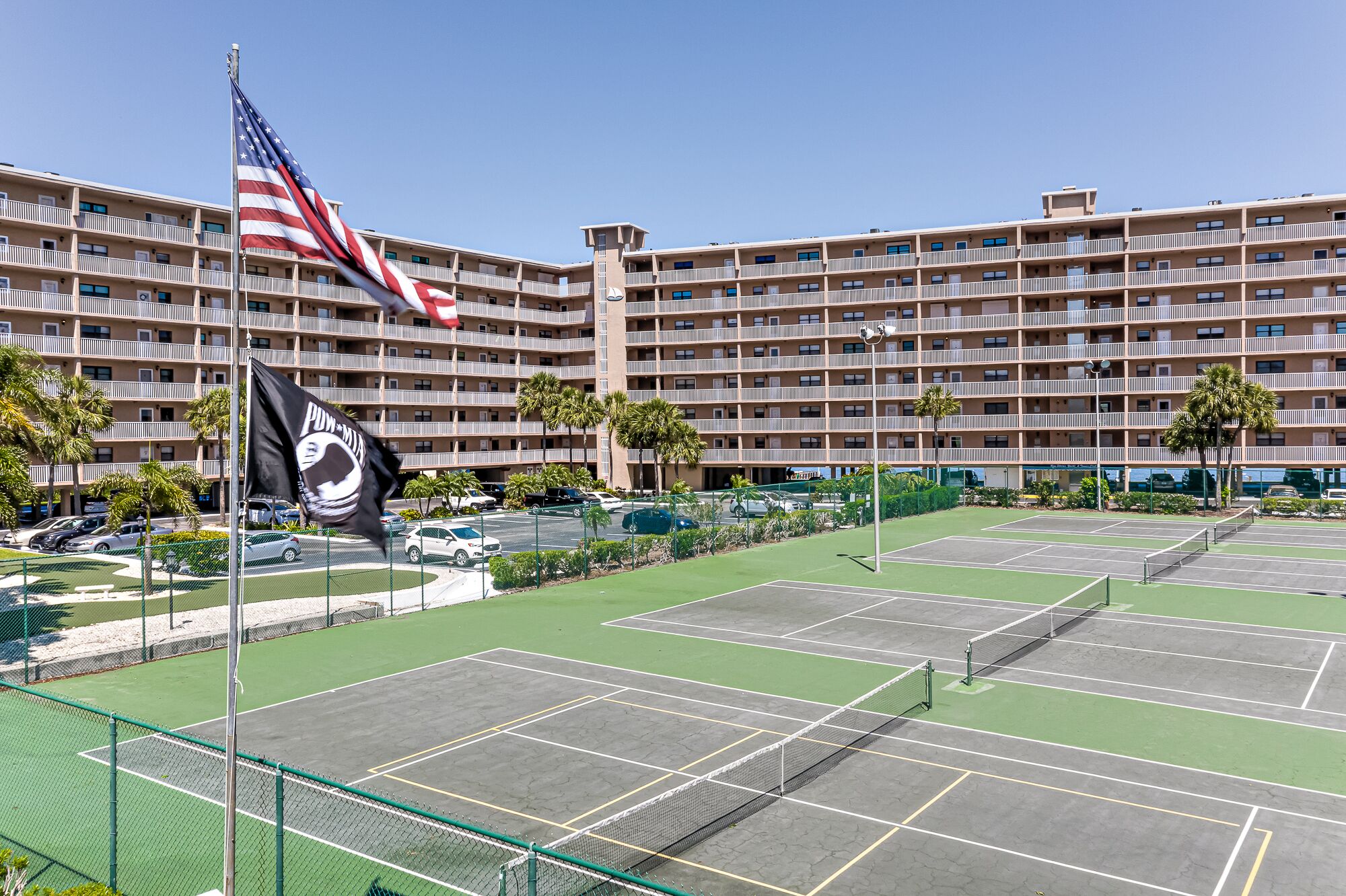 A multi-story hotel with balconies, a tennis court, and a parking area.