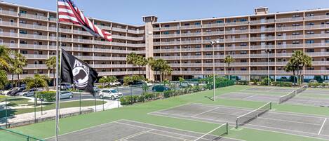 A multi-story hotel with balconies, a tennis court, and a parking area.
