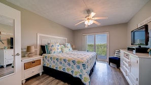A bedroom with a bed, a ceiling fan, a TV, and a balcony with a view.