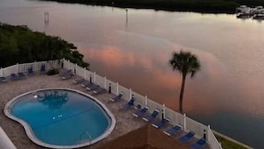 A swimming pool with lounge chairs and a view of a body of water during sunset.