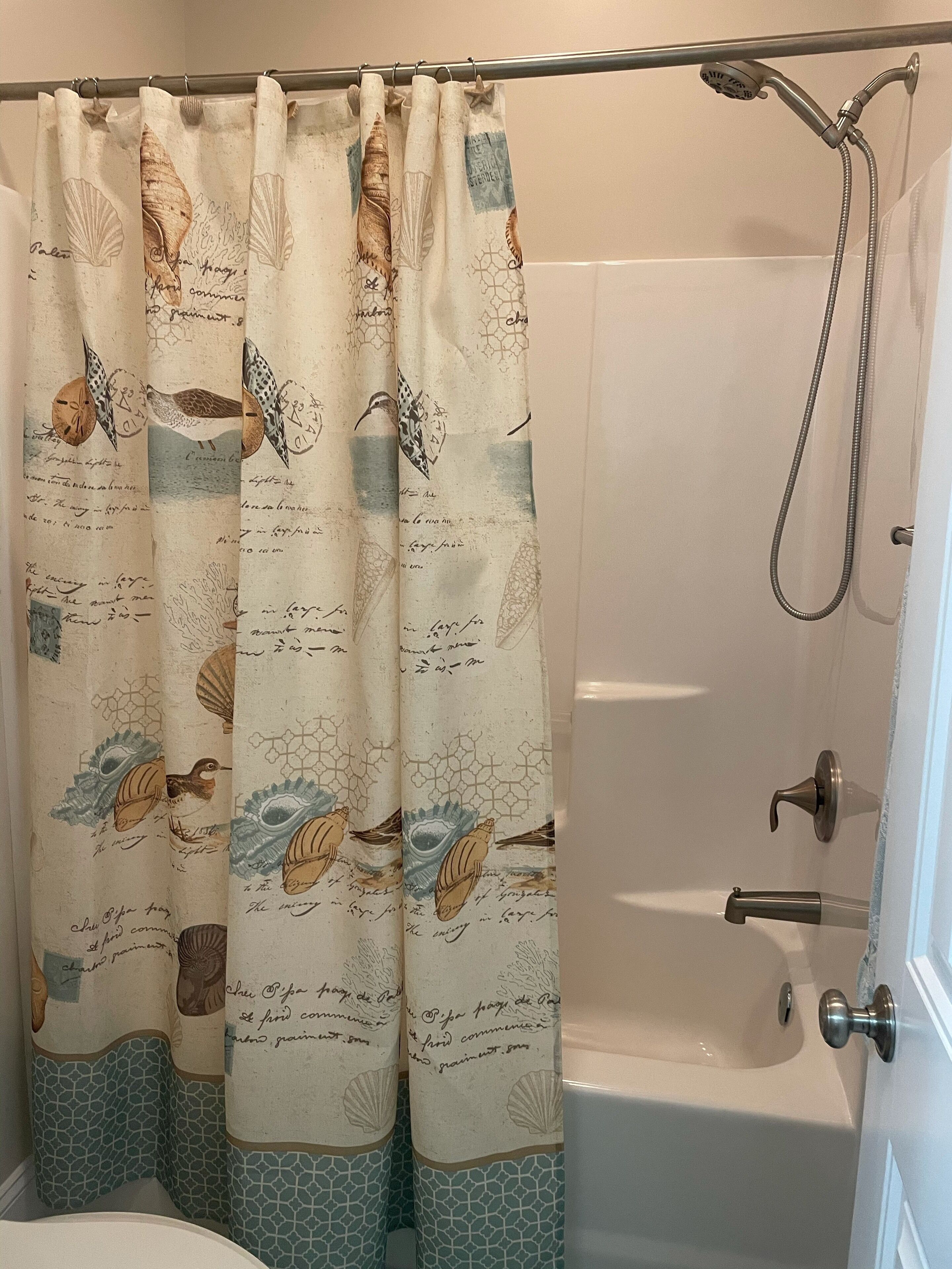 A bathroom with a shower curtain featuring sea creatures and text, a bathtub, and a showerhead.