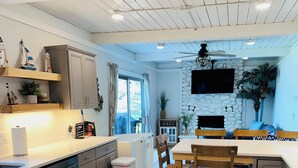 A modern kitchen with wooden flooring, built-in appliances, and a dining area with a stone wall and television. - The Perfect Lake Getaway! (Paw Paw)