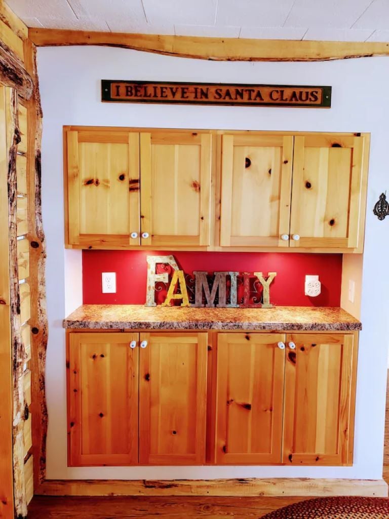 Una cucina con mobili in legno e un piano di lavoro rosso. Sopra il piano di lavoro, un cartello con su scritto "I BELIEVE IN SANTA CLAUS".