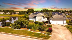 A residential house with solar panels on the roof, a pond, and well-maintained landscaping.