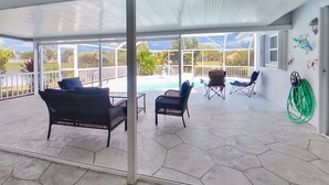 A covered patio with hexagonal stone flooring, wicker furniture, and a view of a swimming pool.