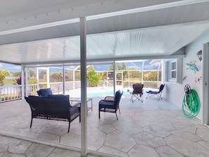 A covered patio with hexagonal stone flooring, wicker furniture, and a view of a swimming pool.