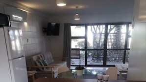 Una cocina con un refrigerador blanco, una mesa de comedor con sillas y vistas al exterior a través de amplias ventanas.