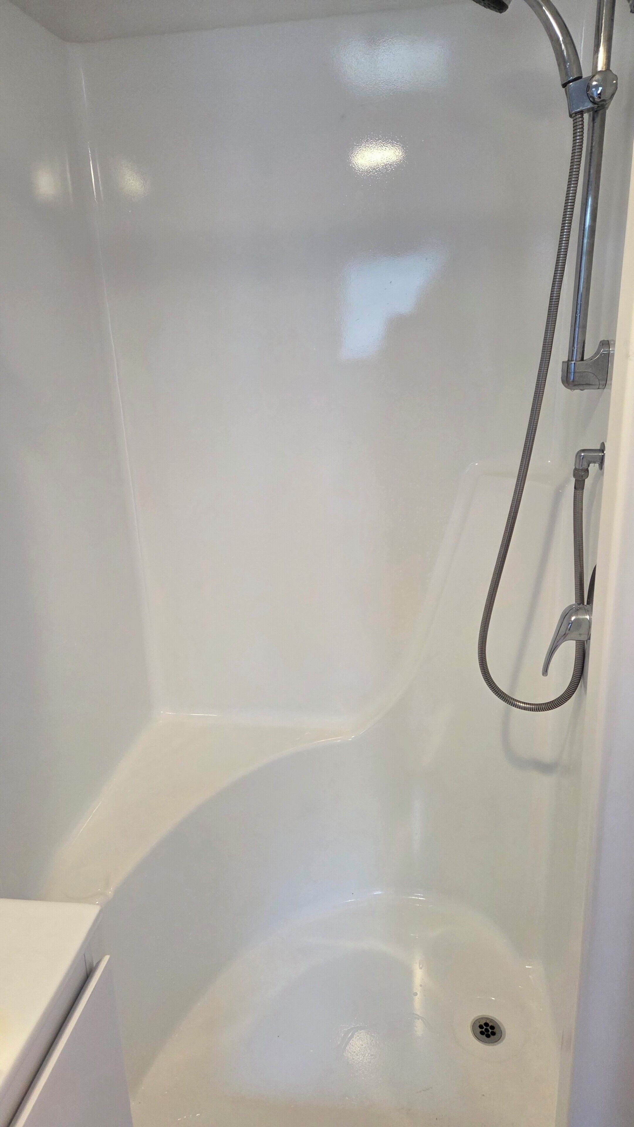 Eine Badewanne mit Duschkopf und Brausearmaturen, einem Abfluss und einer weißen Wand.