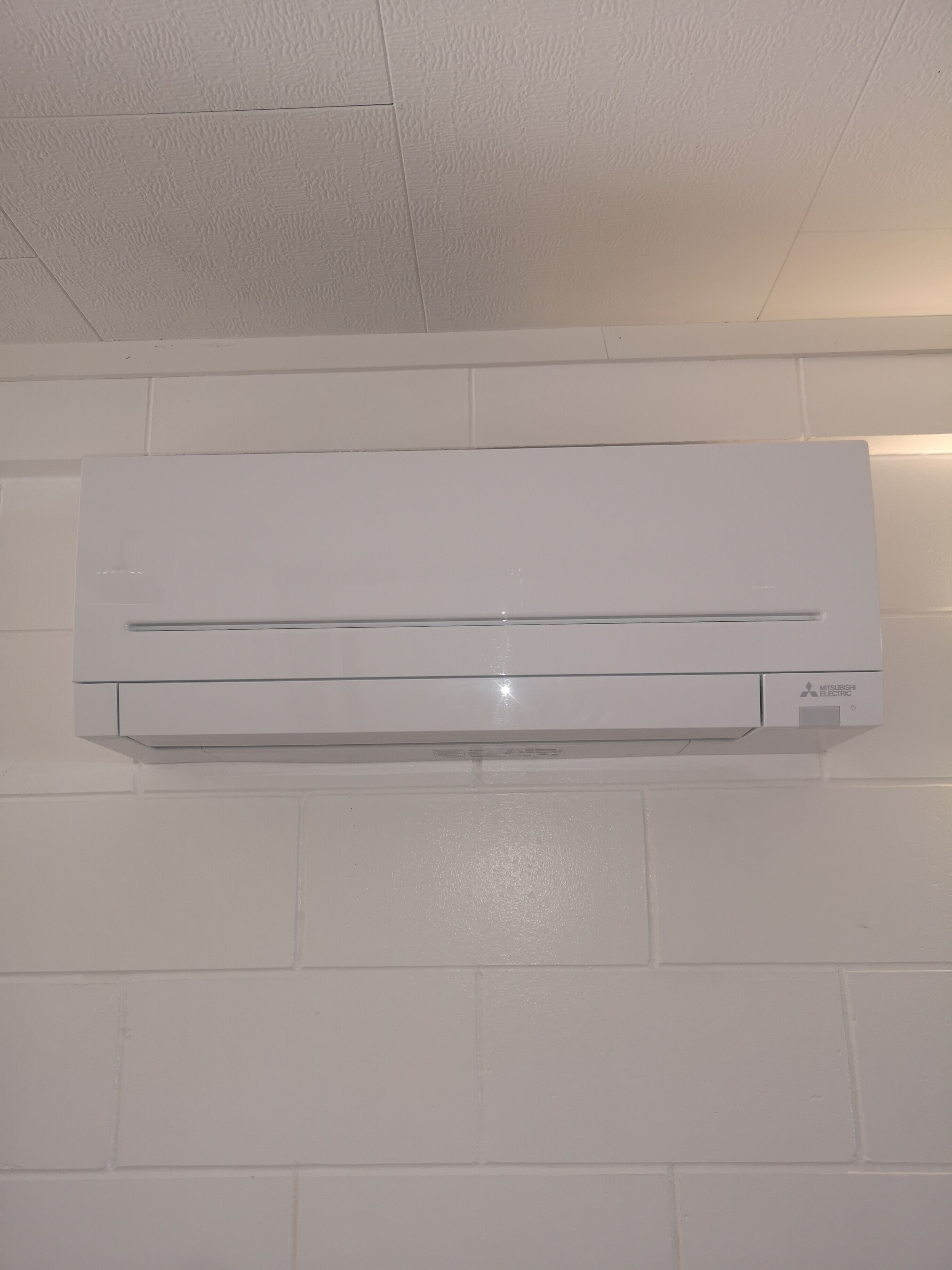 Un appareil de climatisation blanc est fixé sur un mur en briques blanches.