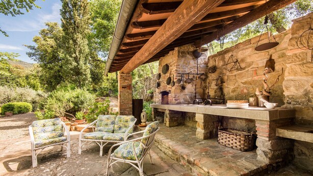 An outdoor kitchen area with stone walls, a wooden pergola, and wicker chairs.