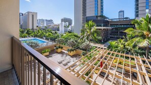 A balcony with a pool, surrounded by lush greenery and tall buildings in the background.