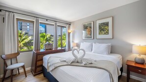 A hotel room with a large bed, a chair, a nightstand, and a view of palm trees through the window.