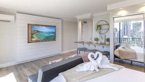 A modern hotel room with a large bed, a desk, a chair, a sofa, a painting, and a city view. - Partial Ocean View King STUDIO with Kitchenette and FREE WIFI! (Honolulu)
