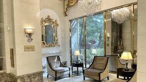 A lobby with two armchairs, a chandelier, and a large mirror reflecting a tropical garden view. - Partial Ocean View King STUDIO with Kitchenette and FREE WIFI! (Honolulu)
