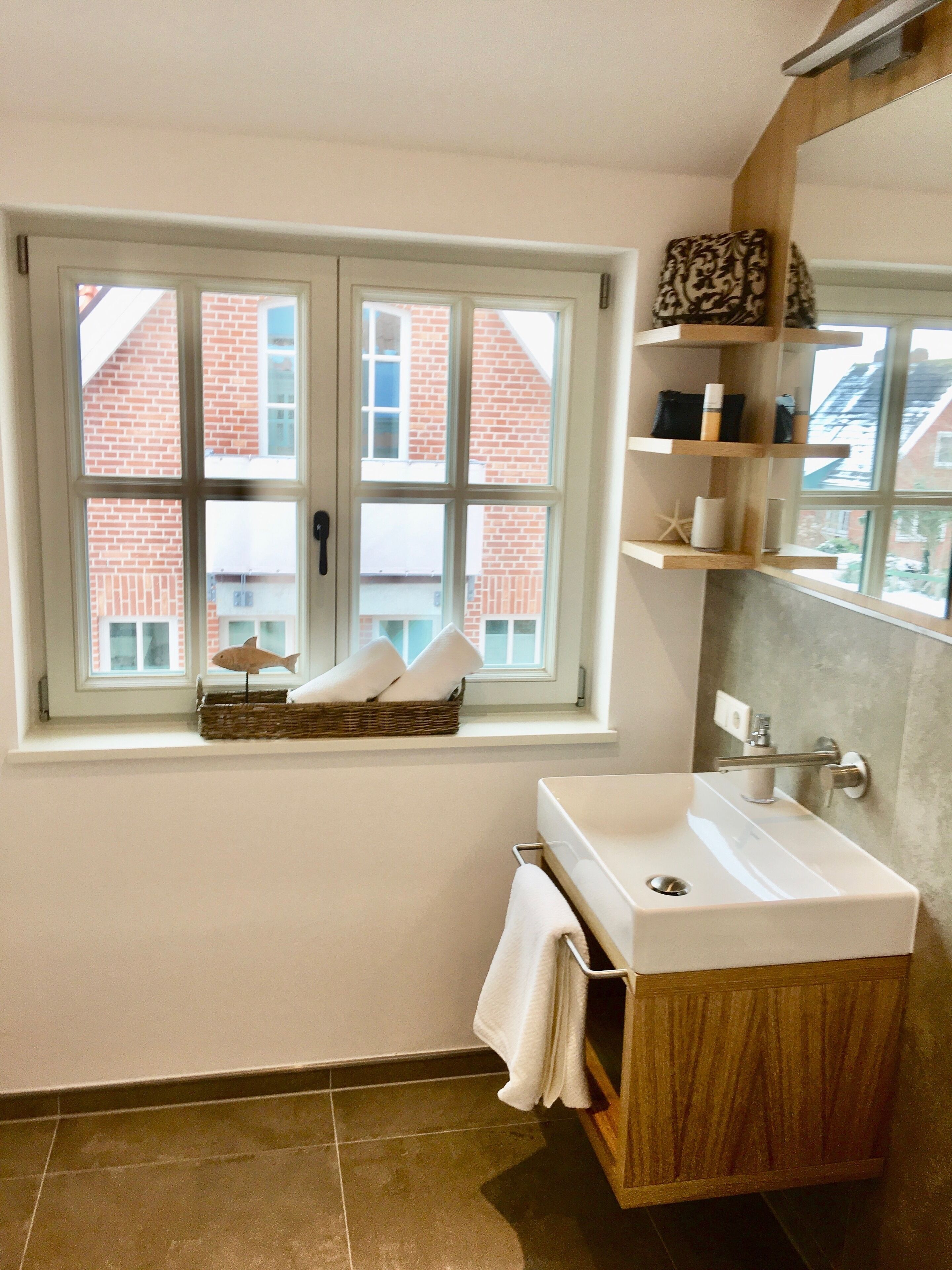 A bathroom with a window, a sink, and a shelf with toiletries.