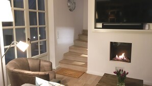 A living room with a sofa, a coffee table, a lamp, a fireplace, a TV, and a staircase.
