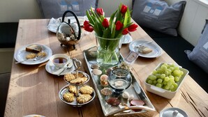 A dining table set with various foods and drinks, a vase with red tulips, and a note with German text.