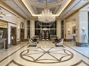A grand lobby with a chandelier, marble flooring, and seating areas.