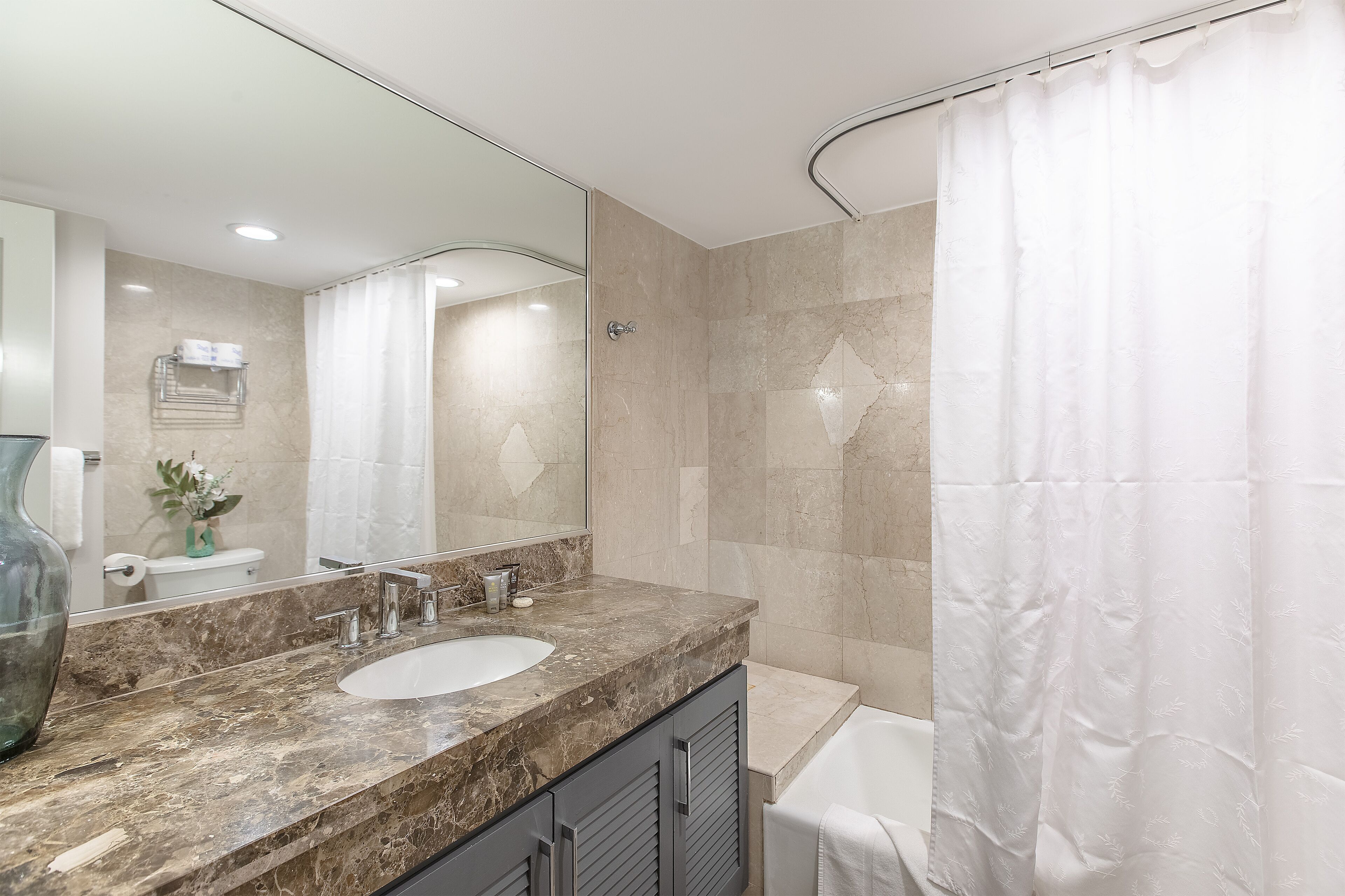 Un bagno moderno con un lavandino in marmo, uno specchio grande e una tenda per la doccia.