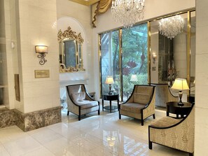 A lobby with two armchairs, a chandelier, and a large mirror reflecting a tropical garden view.