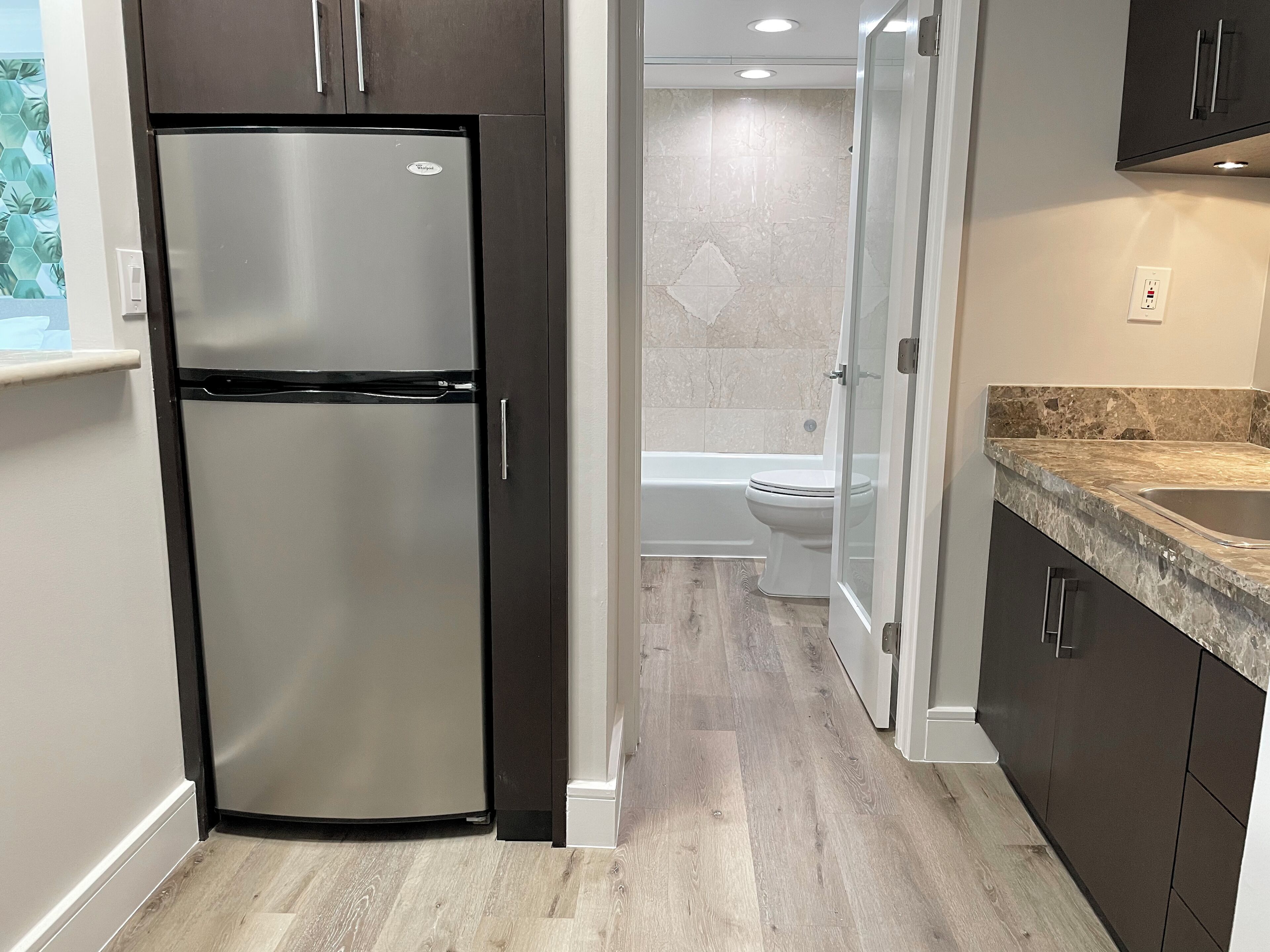 Una cocina moderna con un refrigerador de acero inoxidable, piso de madera y encimera de mármol.
