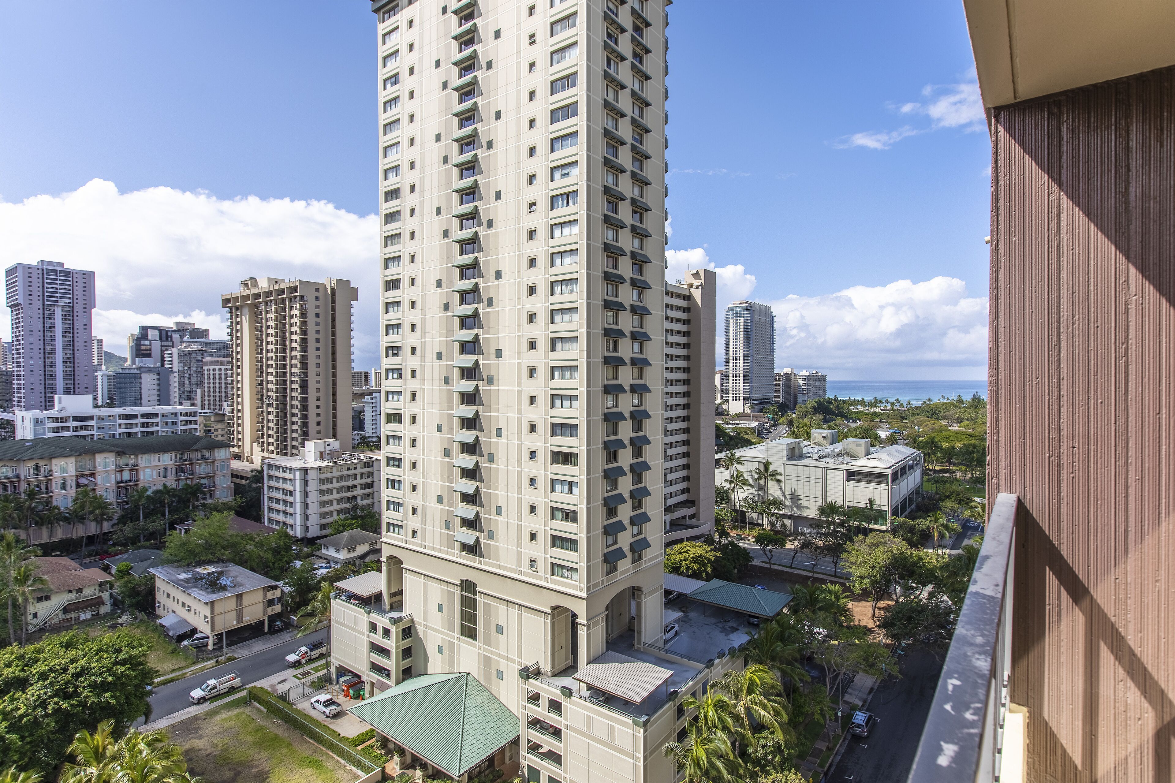 A high-rise building with multiple floors and balconies, surrounded by other buildings and greenery.