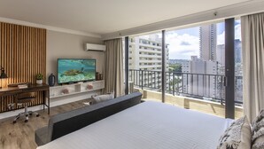 Habitación de hotel moderna con una cama grande, un escritorio con computadora, televisor y balcón con vista a la ciudad.