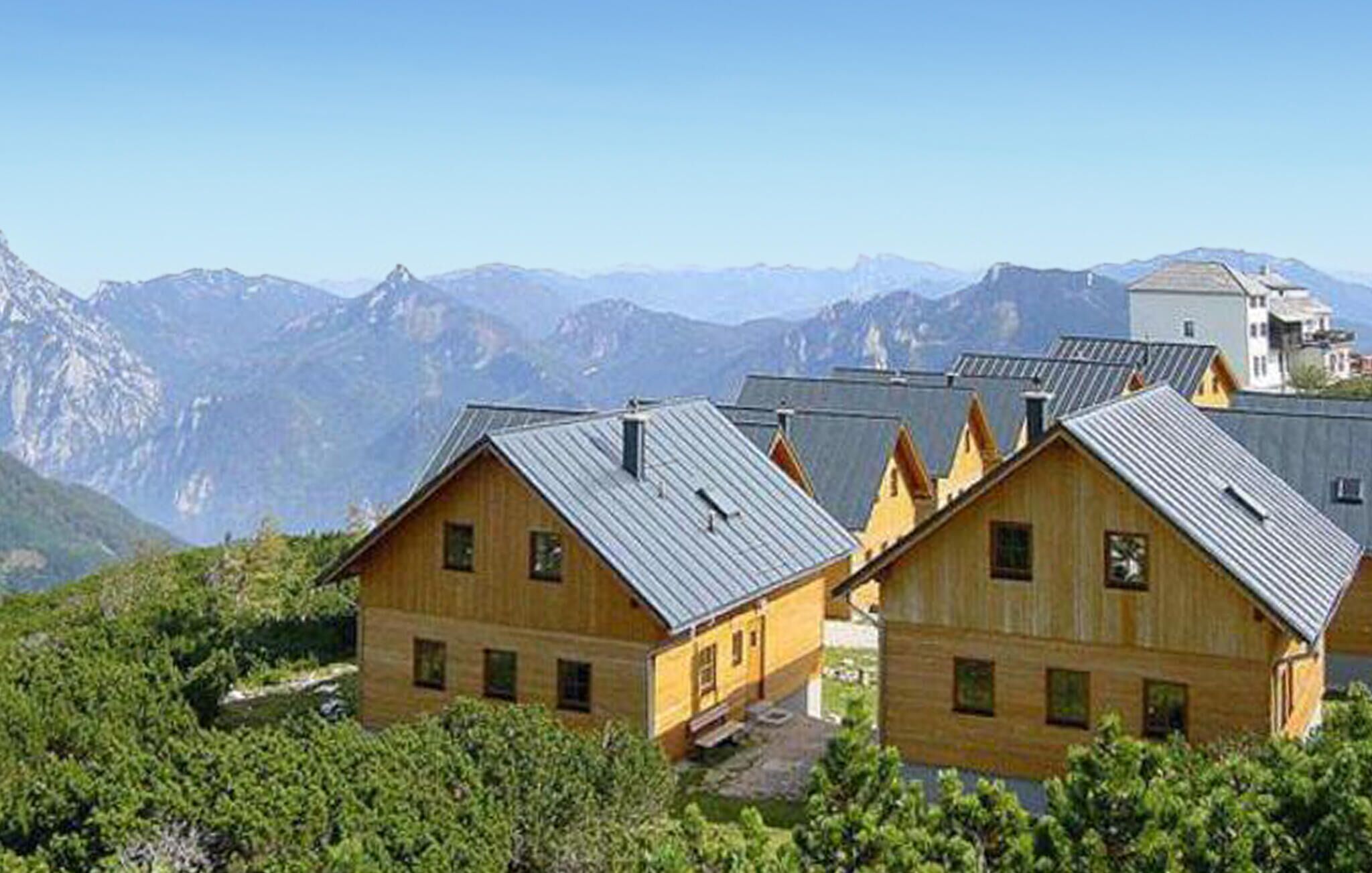Uma fileira de cabanas de madeira com telhados de metal, com montanhas e céu claro ao fundo.
