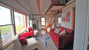Una sala de estar amplia con un sofá rojo, un sillón blanco y una mesa roja. Una escalera conduce a un nivel superior.