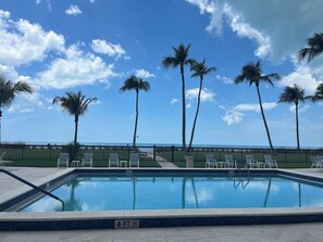 A swimming pool with lounge chairs and palm trees, surrounded by a fence. - Beachfront Vanderbilt Beach Condo in Naples, FL (Naples)