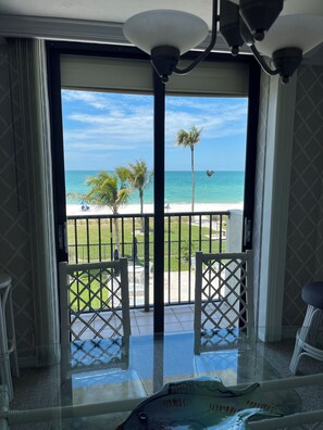 A balcony with a view of the beach and ocean, featuring a glass table and chairs. - Beachfront Vanderbilt Beach Condo in Naples, FL (Naples)