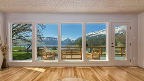 A room with large windows offering mountain views, wooden flooring, and a glass table.