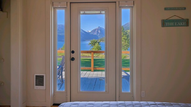 A bedroom with a door leading to a balcony with a view of a lake and mountains.