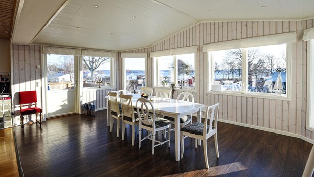 A dining area with a white table and chairs, large windows with a view of the outside, and wooden floors. - Lovely home in Hakenäset with sauna (Hakenäset)