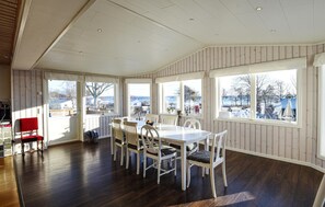 Enjoy a room with a high ceiling, large windows offering views of the outdoors, a wooden floor, and a dining area with a table and chairs.