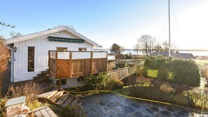 A white building with a wooden deck and a stone pathway leading to a dock. - Lovely home in Hakenäset with sauna (Hakenäset)