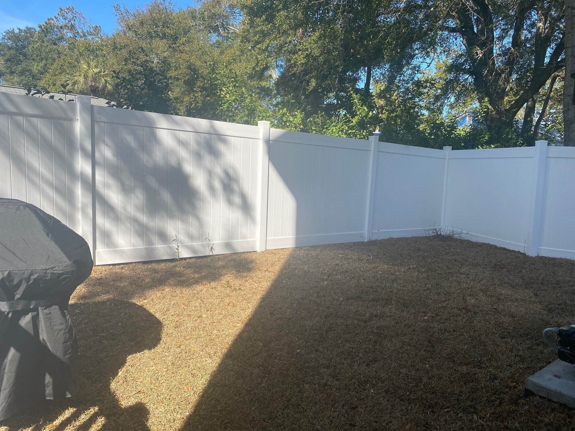 Un jardin avec une clôture blanche, un barbecue et un souffleur de feuilles.