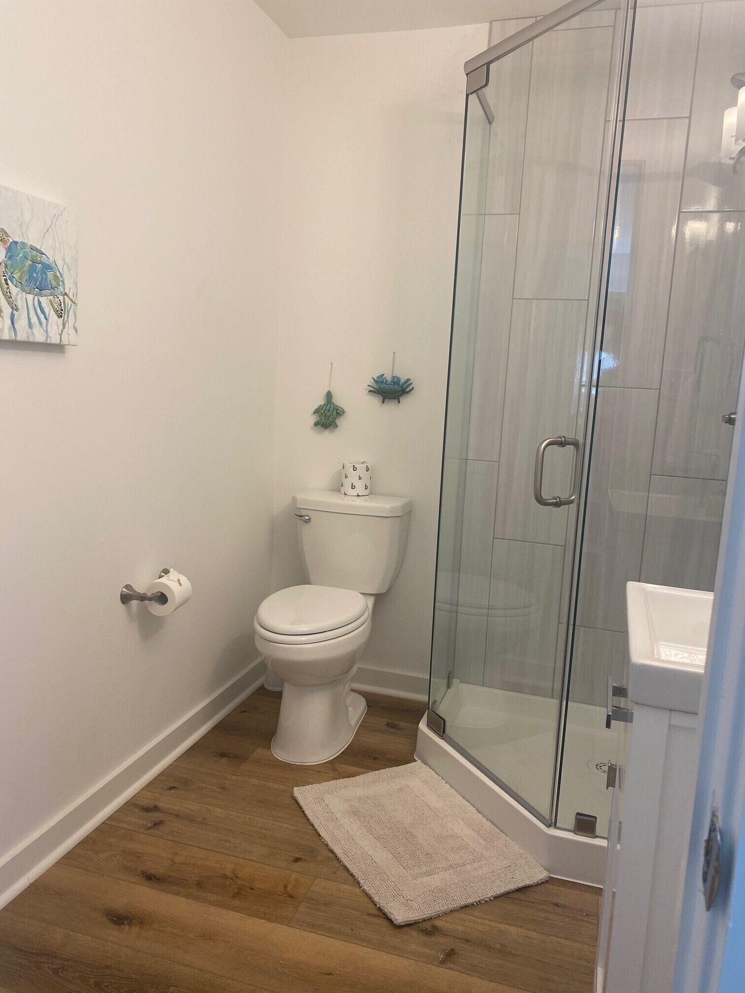 A bathroom with a toilet, a glass shower enclosure, and a wooden floor.