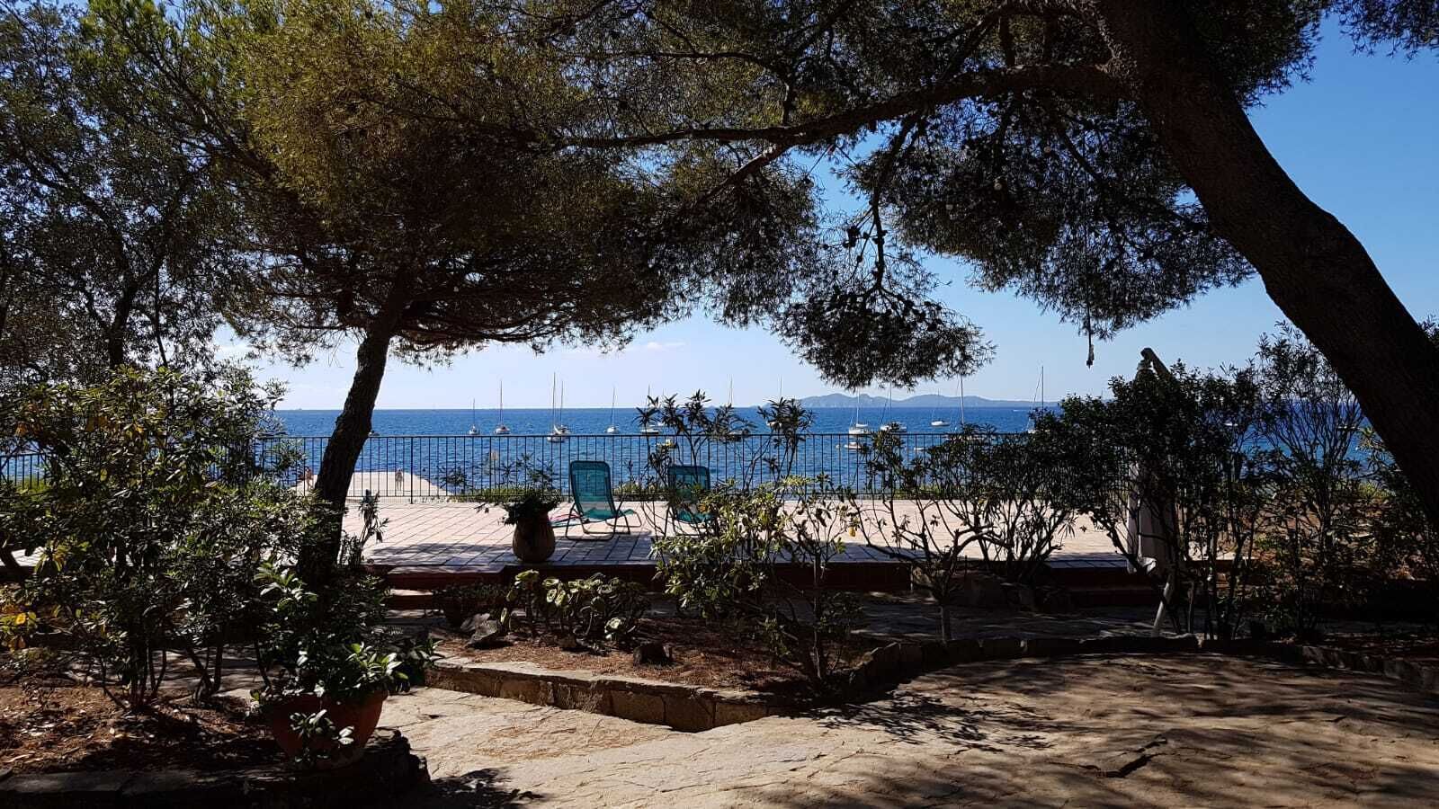 A beachside patio with a view of the sea, surrounded by trees and a fence.